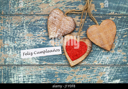 Feliz Cumpleanos (Happy Birthday auf Spanisch) mit drei Holzherzen Stockfoto