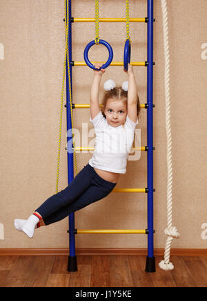 Kleines Mädchen in Sportkleidung Übungen auf Sport Ringen an der schwedischen Wand. Das Konzept einer gesunden Lebensweise von einem jungen Alter. Kinder Sport. Stockfoto