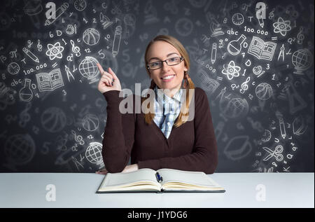 süße Studentin Standortwahl vorne offenes Buch mit illustrierten Schule Tools im Hintergrund Stockfoto