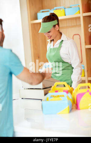 Mann mit Geldschein in Bäckerei an attraktiven weiblichen Verkäufer bezahlen. Stockfoto