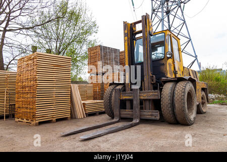 Große Gabelstapler und Stapel von neuen Holzbrettern und Nieten an den Holzplatz. Holzplatten auf Pfählen für Möbel-Materialien Stockfoto