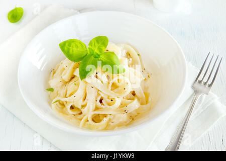 Alfredo-Tagliatelle-Nudeln mit Basilikum und schwarzem Pfeffer in weiße Schüssel - hausgemachte cremige Pasta mit Alfredo Soße Stockfoto