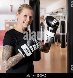 Junge Frau, tätowiert, Boxen an einem Sandsack in einem Box-Studio, Bayern, Deutschland Stockfoto