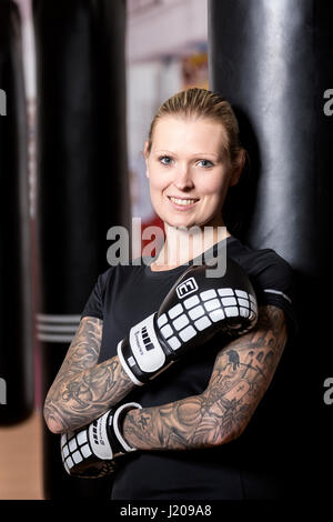 Junge Frau, tätowiert, Boxen an einem Sandsack in einem Box-Studio, Bayern, Deutschland Stockfoto