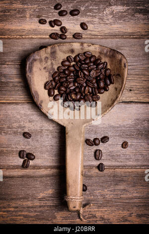 Draufsicht der dunkle Röstung der Kaffeebohnen in antiken hölzernen Schaufel, am alten Holz Hintergrund. Stockfoto