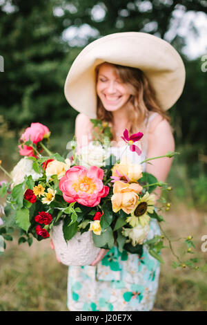 Bouquet, Menschen, Blumen Urlaub, Geschenk und Blumenarrangement Konzept - close-up auf schönen frischen Blumenstrauß, lächelnde junge Frau in ausgefallenen Hut hält Vase mit Sommerblumen in Natur Hintergrund. Stockfoto