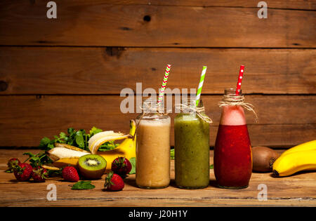 Auswahl an Obst und Gemüse-Smoothies in Glasflaschen mit einem Strohhalm auf hölzernen Hintergrund. Stockfoto