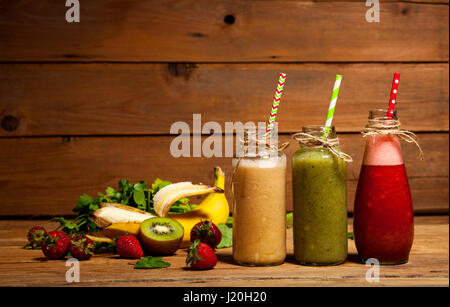 Auswahl an Obst und Gemüse-Smoothies in Glasflaschen mit einem Strohhalm auf hölzernen Hintergrund. Stockfoto