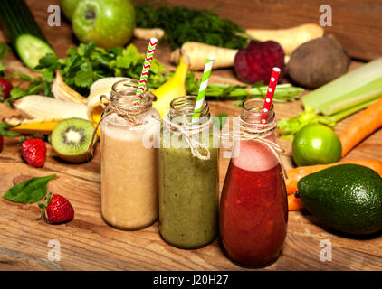 Auswahl an Obst und Gemüse-Smoothies in Glasflaschen mit einem Strohhalm auf hölzernen Hintergrund. Stockfoto