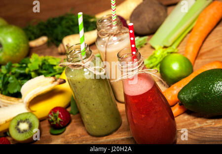 Auswahl an Obst und Gemüse-Smoothies in Glasflaschen mit einem Strohhalm auf hölzernen Hintergrund. Stockfoto