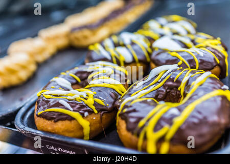 Makro Nahaufnahme von Schokolade bedeckt glasiert Geeiste Donuts mit beträufelt gelbe Sirup Stockfoto