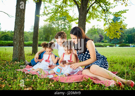 Happy Family im Park Sommer, Herbst. Eltern und zwei Töchtern sitzen, spielen. Stockfoto