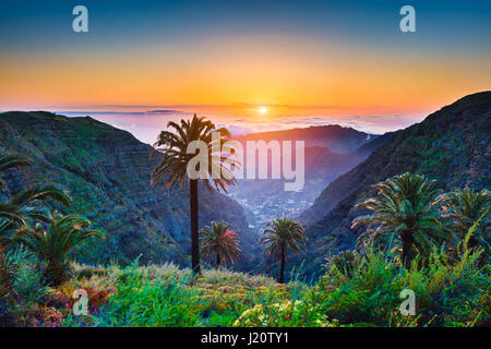 Schöne Aussicht auf atemberaubende tropische Landschaft mit exotischen Palmen und Bergtäler über weite Meer im goldenen Abendlicht bei Sonnenuntergang Stockfoto