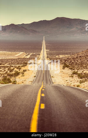 Klassische vertikale Ansicht einer endlosen geraden Straße laufen durch die karge Landschaft des amerikanischen Südwestens mit extremer Hitze Dunst im Sommer Stockfoto