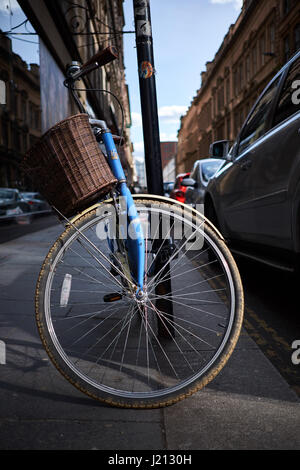 Blaues Fahrrad mit Korb ruht gegen einen Beitrag auf einer Straße, die von nachmittags Sonnenlicht beleuchtet Stockfoto