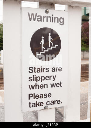 eine Warnung, dass Schild mit der Aufschrift, dass Treppen rutschig sind, wenn nass Bitte achten Sie in der Nähe von Zug Brücke Schritte oben vorsichtig Sicherheitshinweise advisory verfolgen Stockfoto