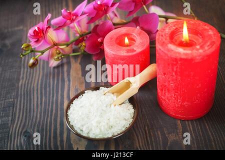 Meer-Badesalz, Kerzen und Blumen auf einem hölzernen Hintergrund. Das Konzept der Entspannung und Wellness. Stockfoto