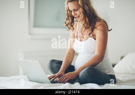 Werdende und glücklich Schwangere mit Technologie von zu Hause aus Stockfoto