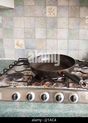 Eine große schwarze Runde Runde Pfanne ohne jegliche Nahrung auf der Oberseite Herd Gasherd mit wählt alle ausschalten und mit Bits von Schmutz und verbranntem Essen eingeschaltet Stockfoto