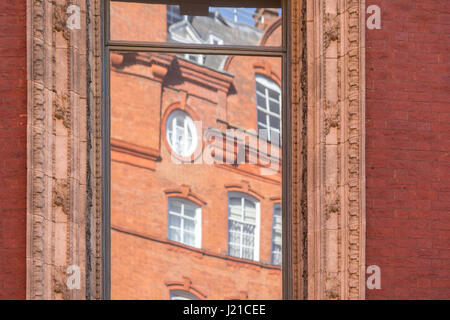 Reflektion von einem alten Backsteingebäude in London in einem Fenster mit kunstvollen Formen, London, England, Grossbritannien Stockfoto