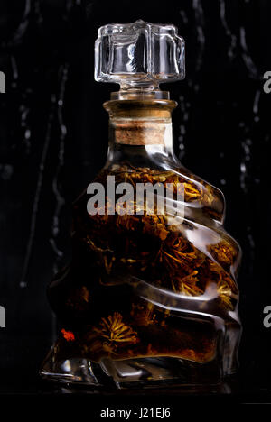 Flasche mit Tinktur auf Blüten auf schwarzem Hintergrund Stockfoto