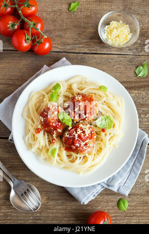 Spaghetti Nudeln mit Fleischbällchen, Tomatensauce, geriebenem Parmesan und frischem Basilikum - gesunde hausgemachte italienische Pasta auf rustikalen hölzernen Hintergrund mit Stockfoto