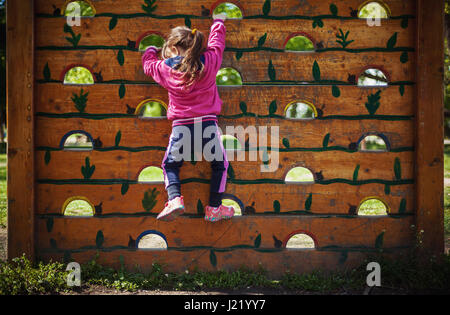 Kleines Mädchen klettert auf einer Holzwand im Park. Stockfoto