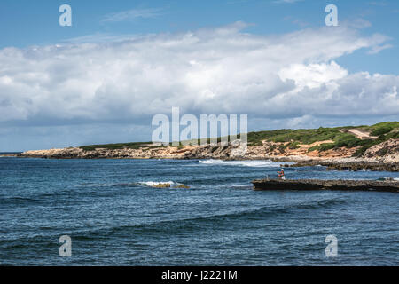 Capo Mannu Cliffs in Sardinien, Italien gegen türkisblauen Meer oder Ozean mit blauem Himmel und dramatische Wolken mit unkenntlich Fischer. Stockfoto