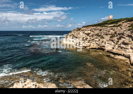 Capo Mannu Cliffs in Sardinien, Italien gegen türkisblauen Meer oder Ozean mit blauen Himmel und dramatische Wolken. Alten Wachturm im Hintergrund. Stockfoto