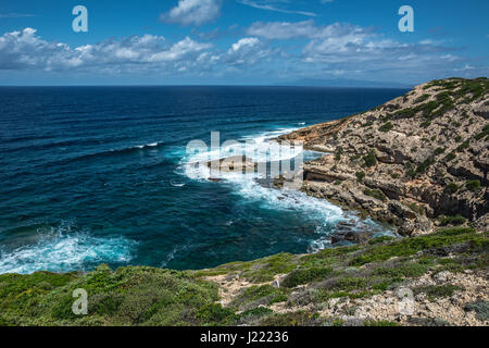 Capo Mannu Cliffs in Sardinien, Italien gegen türkisblauen Meer oder Ozean mit blauen Himmel und dramatische Wolken. Wellen gegen Felsen. Stockfoto