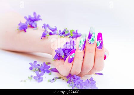 Hand mit Nägeln wieder aufgebaut und geschmückt mit bunten Blumen bringen blauen und weißen Blumen auf weißem Hintergrund, schöne Neuheit für Frühling und Sommer Stockfoto