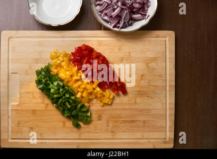 Geschnittenen frischen Paprika Stücke Top-down Ansicht auf einem Bambus-Schneidebrett mit geschnittenen Zwiebeln. Ohne Hand. Stockfoto