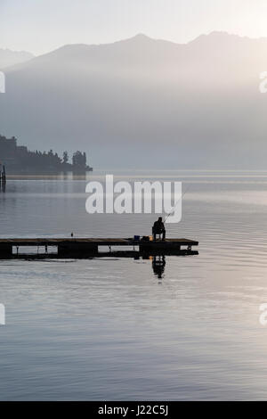 Einsamen Fischer sitzt auf Steg Angeln an einem frühen nebligen Morgen in Lenno, Comer See, Italien im April Stockfoto