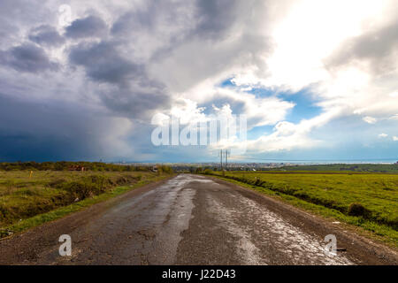 Alte Risse Straße nach Regen. Schlechten holprigen Straße mit Löchern und stürmischen bewölkten Himmel. Stockfoto