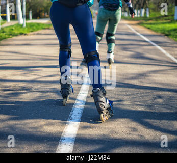 Zwei Mädchen auf Rollschuhen fahren entlang der Straße nebeneinander Stockfoto