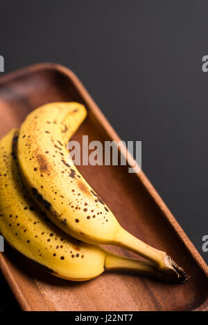 Zwei Bio-Bananen in einem Holz über ein schwarzes Brett. Stockfoto