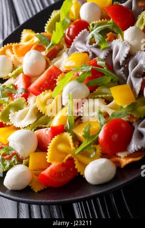 Warmer Salat von Farfalle Nudeln, Tomaten, Rucola und Mozzarella Closeup auf einem Teller. vertikale Stockfoto