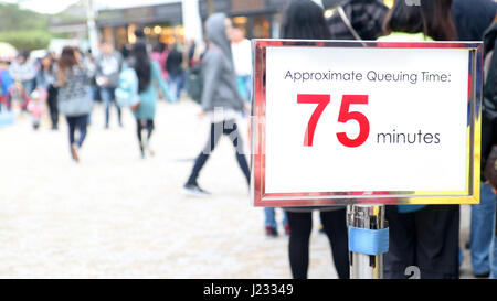 Menschen warten in einer langen Schlange, Fokus auf dem Hinweisschild. Plakat mit Informationen über die Wartezeit neben Linie mit vielen Menschen warten. Stockfoto