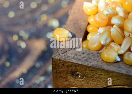 Eine Mais-Bohne am Rande eine hölzerne Truhe voller Mais Bohnen. Natürliches Licht, hölzerne Tabelle. Stockfoto