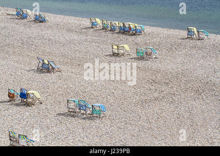 Blick von einem hohen Winkel auf der einsamen Kiesstrand an Bier in Devon, UK mit leeren, gestreiften Liegestühlen verteilt. Stockfoto