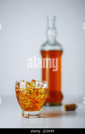 Glas voll Eiswürfel und alkoholisches Getränk und eine Flasche im Hintergrund Stockfoto