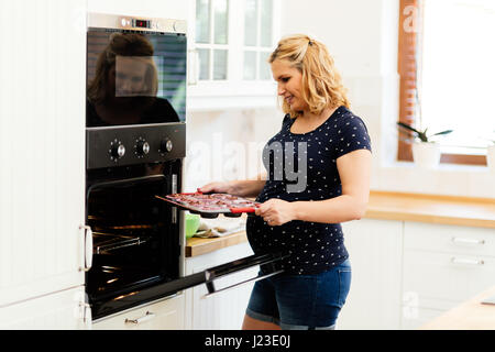 Schöne schwangere Frau Vorbereitung Muffins in Küche Stockfoto