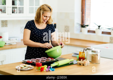 Schöne schwangere Frau Vorbereitung Muffins in Küche Stockfoto