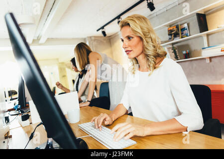 Schöne Frau in einem modernen Büro beim Sitzen vor einem Desktop-PC arbeiten Stockfoto