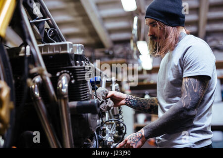 Seite Ansicht Porträt der tätowierte Mann arbeitet in Garage reparieren defekte Motorrad und Anpassung Stockfoto