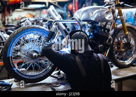 Zurück Blick Porträt der tätowierte Mann mit Schutzmaske Schweißen Motorradrahmen in Werkstatt Stockfoto