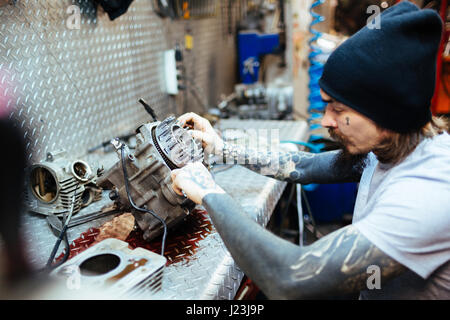 Seite Ansicht Porträt des modernen tätowierte Menschen defekten Motor Befestigungsteile in Werkstatt Stockfoto