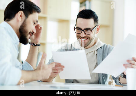 Porträt der beiden mittleren Alters Kollegen arbeiten mit Dokumentation bei Treffen im modernen lichtdurchfluteten Büros und lächelnd Stockfoto