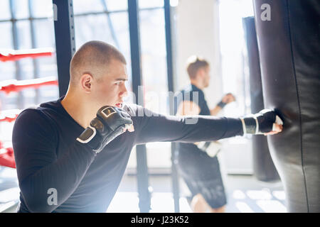 Seite Ansicht Porträt des jungen muskulösen Boxer schlagen Boxsack im sonnendurchfluteten kämpfenden Club üben, Geschwindigkeit und Stärke Stockfoto