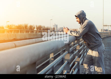 Gut aussehender Mann, ruhen Sie sich nach selbst Training, männliche Läufer mit Handy. Fitness-Konzept Stockfoto